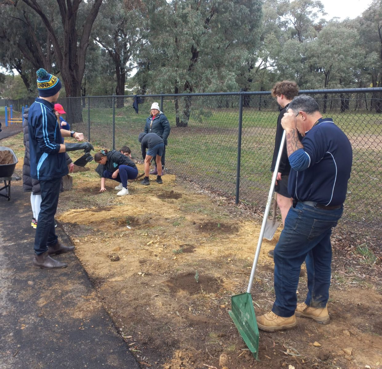 Students planting trees while teacher watches on
